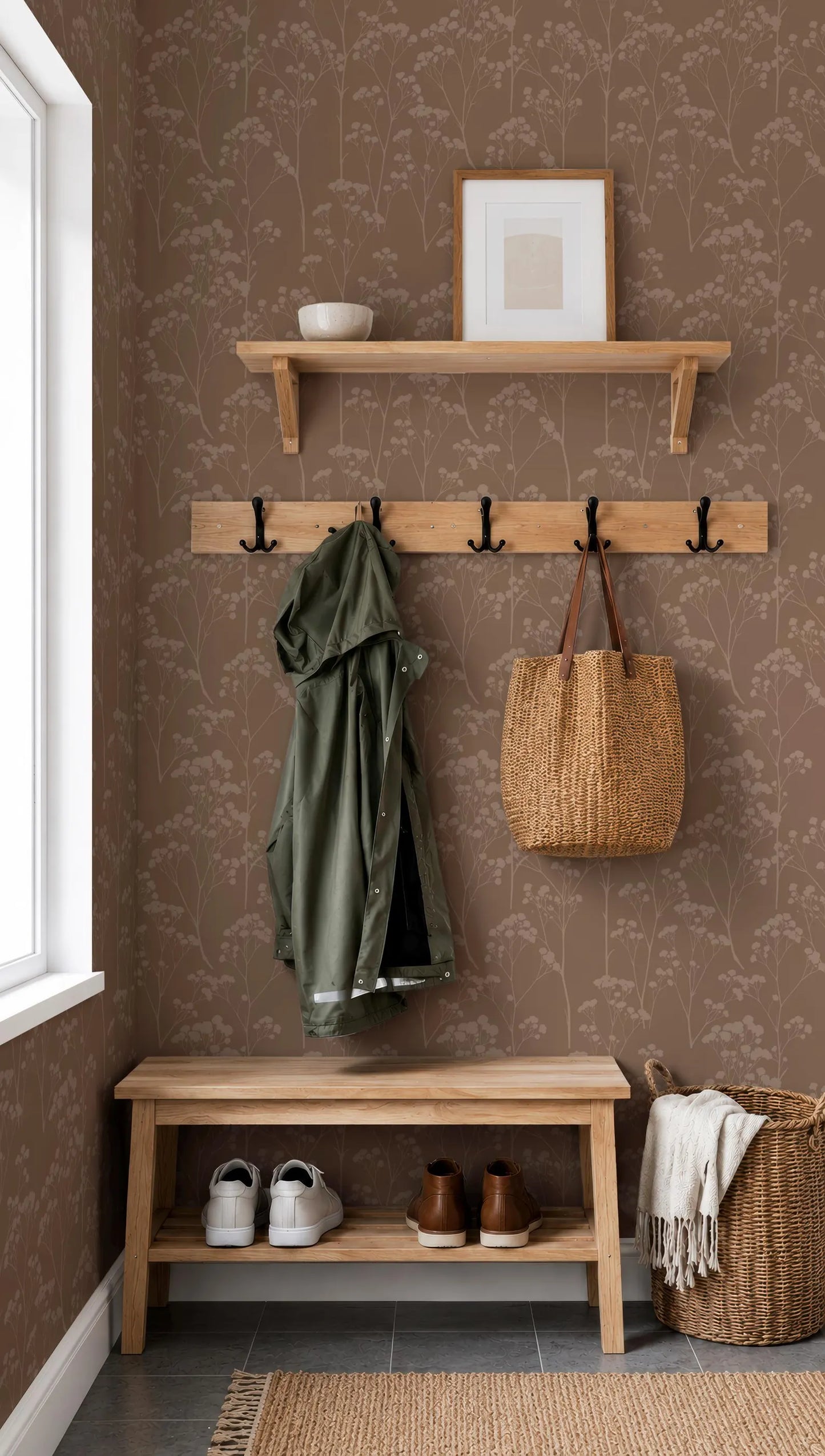 a cozy entryway with a wooden bench, a coat rack, and a shelf with a picture frame. The wall behind the bench has a floral wallpaper, and there are two baskets and a pair of shoes placed on the bench.