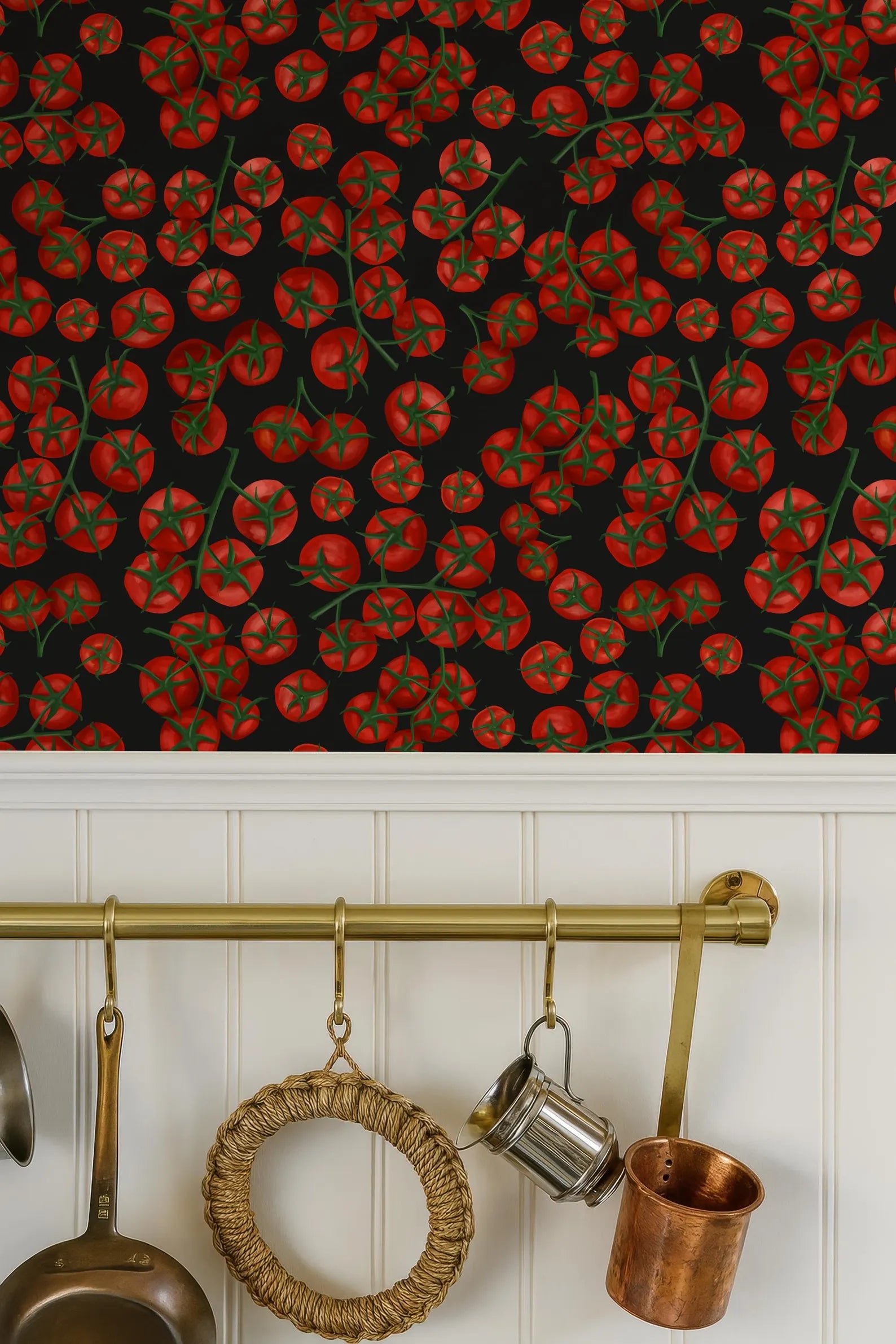 a kitchen scene with a wallpapered background of red tomatoes, a brass rack with various kitchen utensils hanging on it, and a copper pot below the rack.
