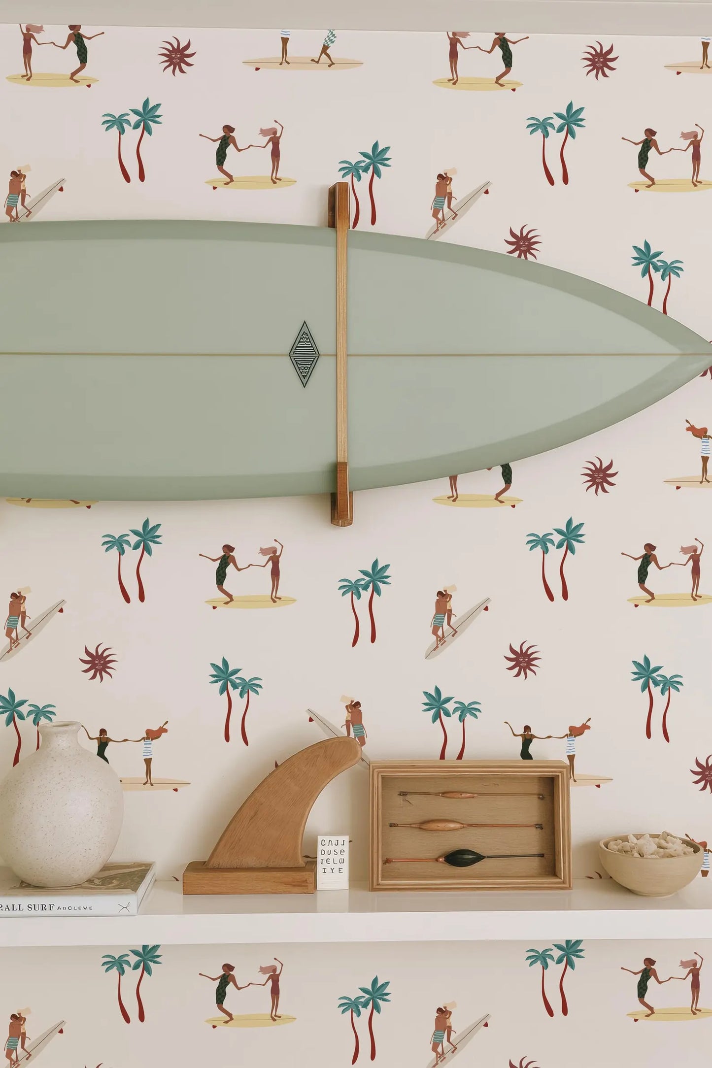 a wallpapered wall with a surfboard hanging on it, along with various decorative items such as a wooden sculpture, a bowl, and a book.