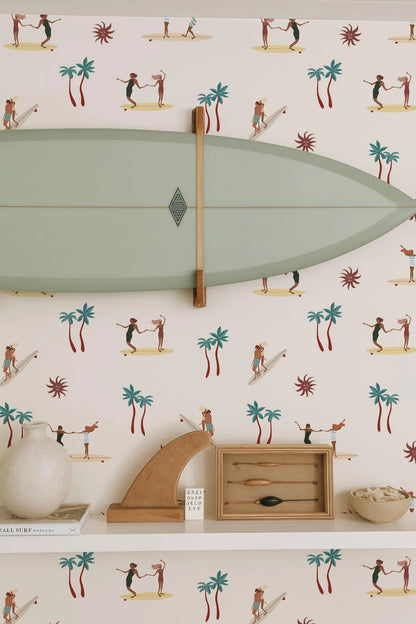 a wallpapered wall with a surfboard hanging on it, along with various decorative items such as a wooden sculpture, a bowl, and a book.