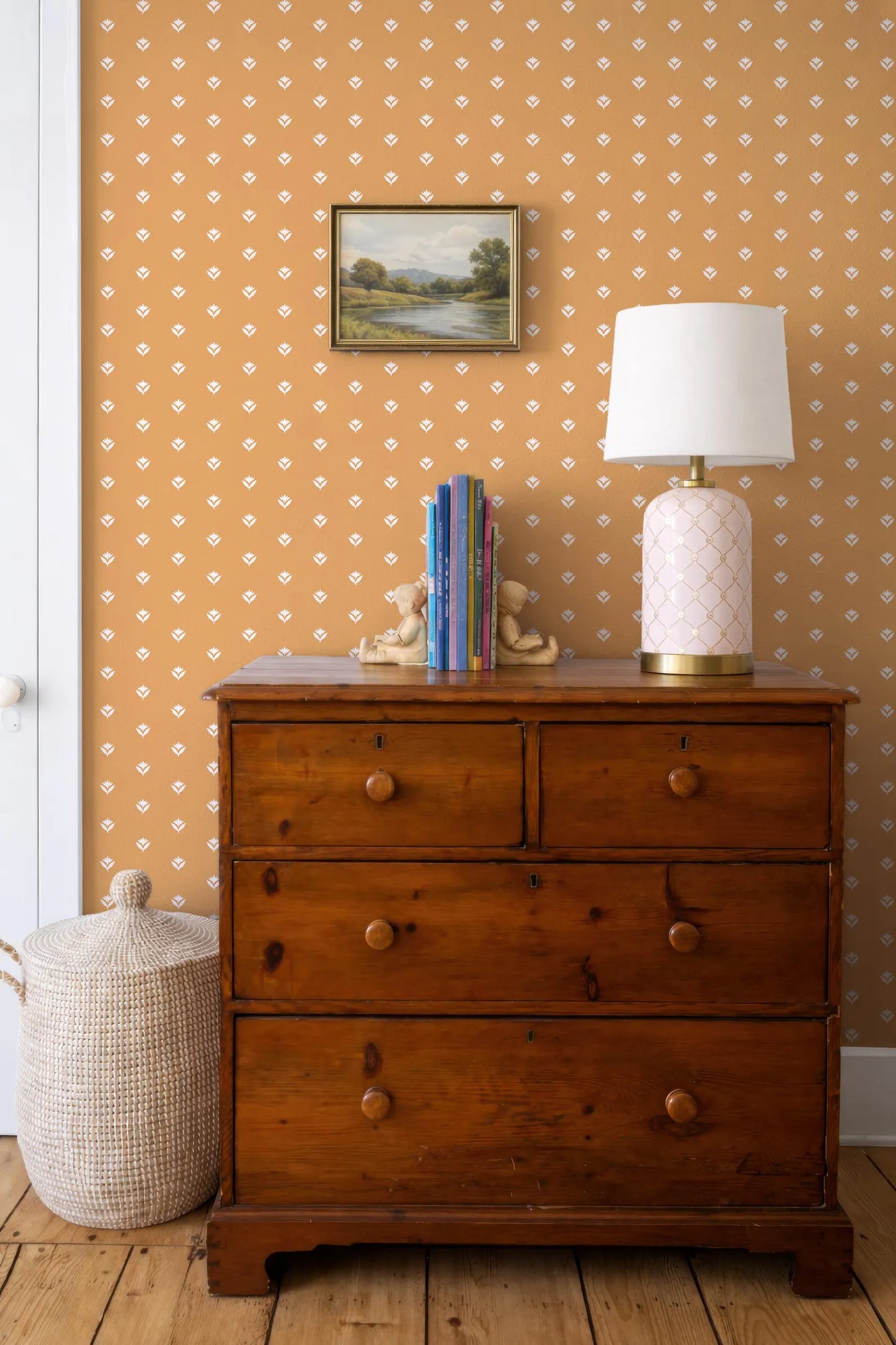 a wooden dresser with a lamp and a basket on top, set against a wall with a patterned wallpaper.