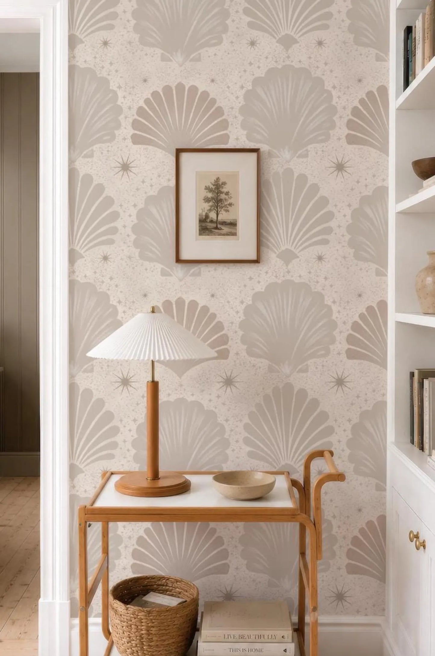 a cozy corner of a room with a wooden table, a lamp, and a framed picture on the wall. The wall has a repeating pattern of seashells and stars, creating a warm and inviting atmosphere.