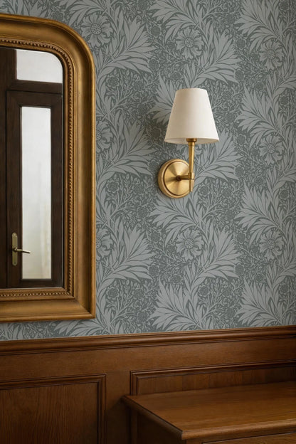 a wallpapered wall with a gold-framed mirror and a gold-framed wall lamp.