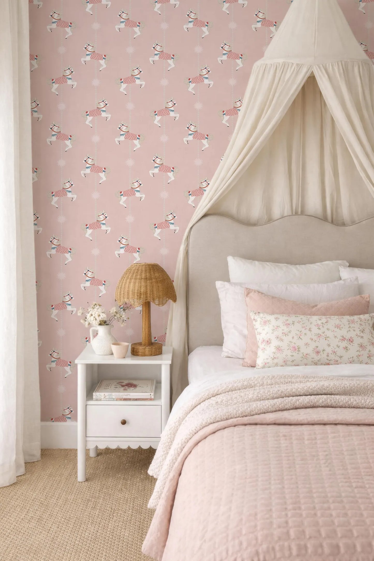 a cozy and charming bedroom with a pink and white color scheme. The focal point is a bed with a canopy, and the walls are adorned with a pink wallpaper featuring a playful pattern of horses. The room is further decorated with a white nightstand, a lamp, and a vase of flowers, creating a warm and inviting atmosphere.