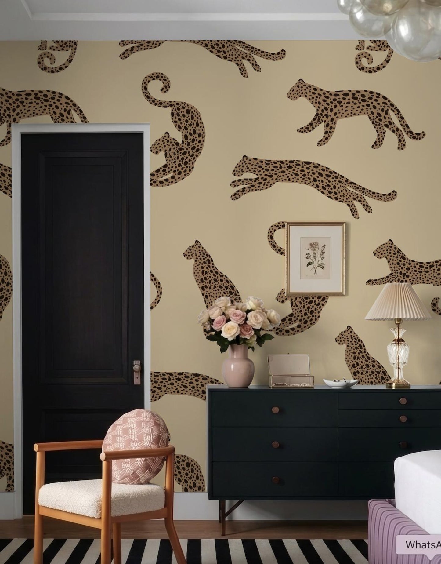 a room with a black door, a dresser with a vase of flowers, and a chair with a pillow. The wall behind the dresser has a repeating pattern of leopard designs in various sizes and orientations.