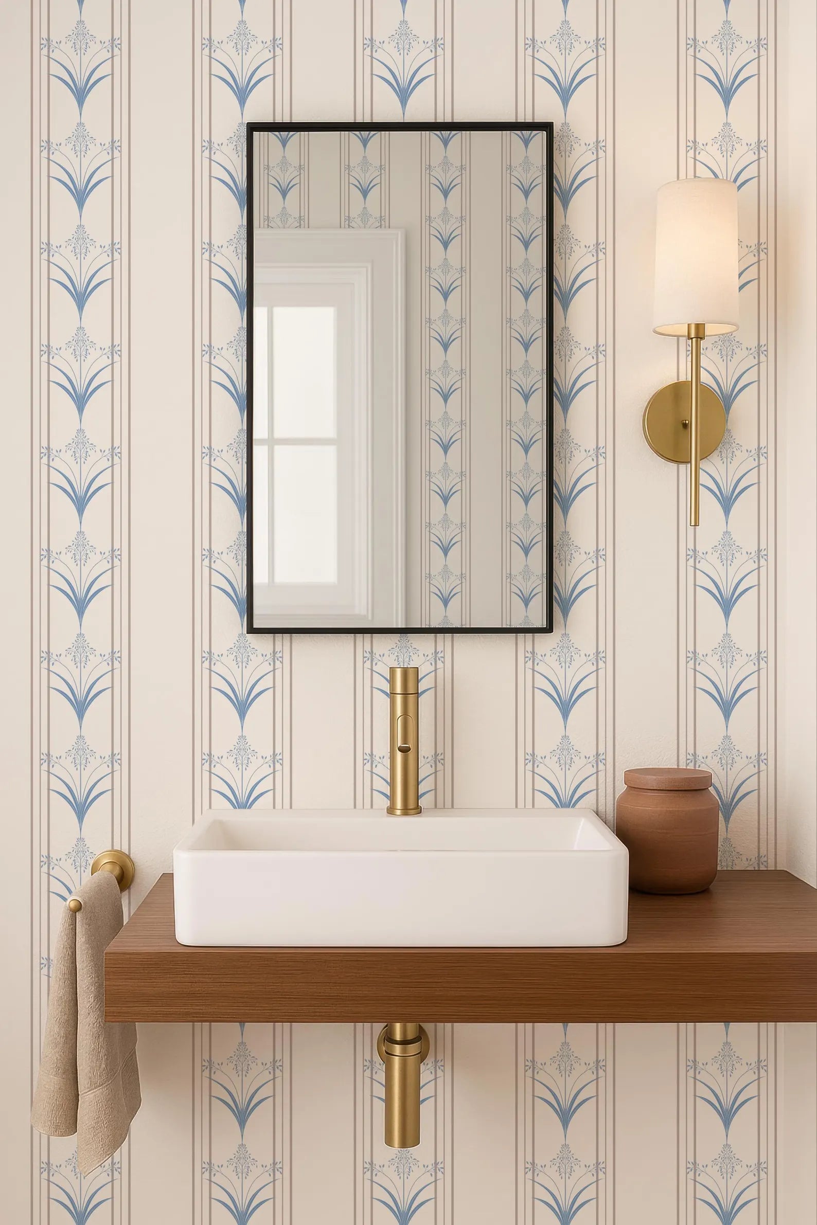 a bathroom with a white rectangular sink, a mirror above it, and a wooden shelf below the sink. The wall behind the sink has a blue and white patterned wallpaper.