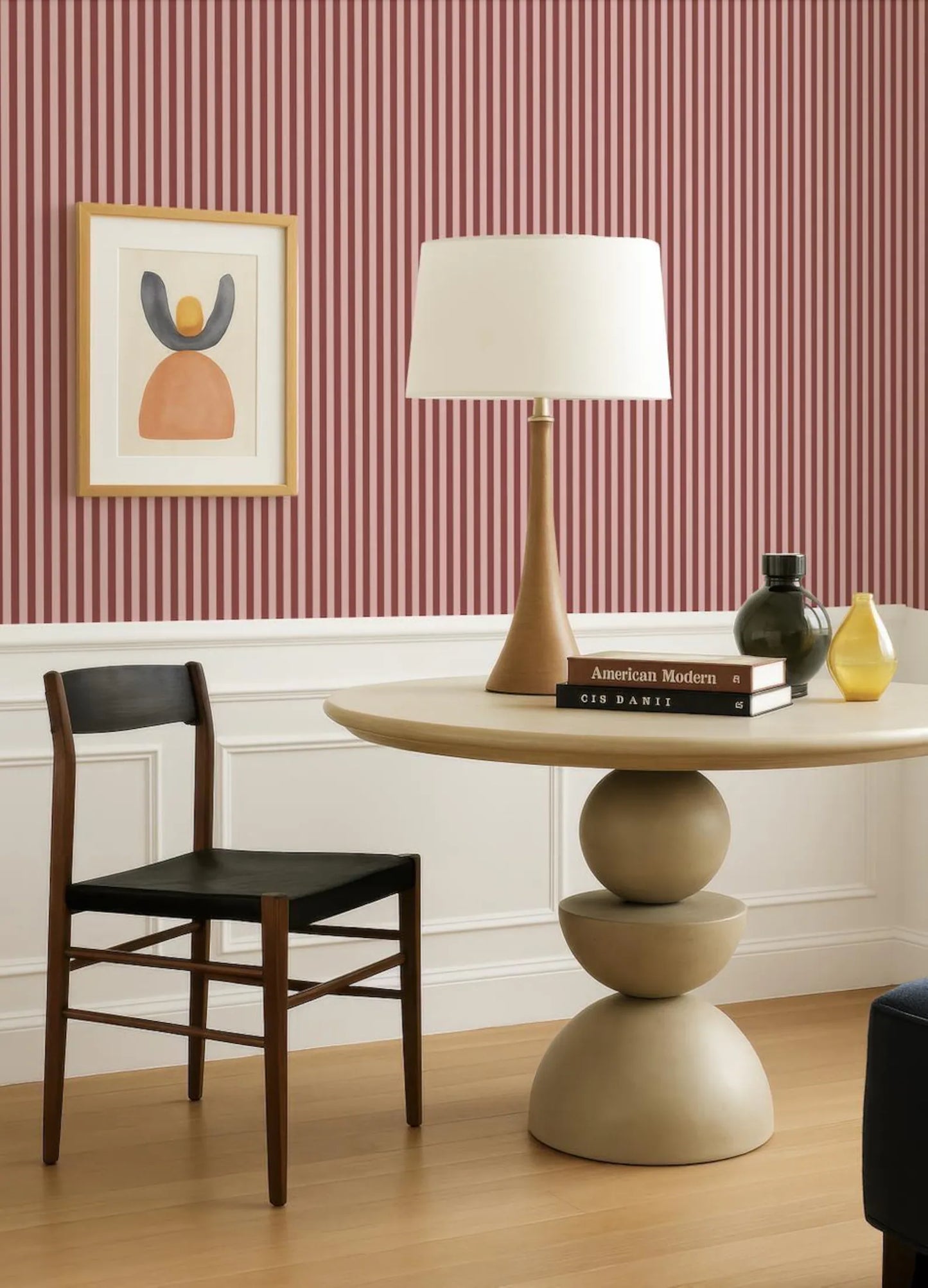 a modern living room with a wooden chair, a round table with a lamp, and a framed artwork on the wall.