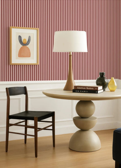 a modern living room with a wooden chair, a round table with a lamp, and a framed artwork on the wall.