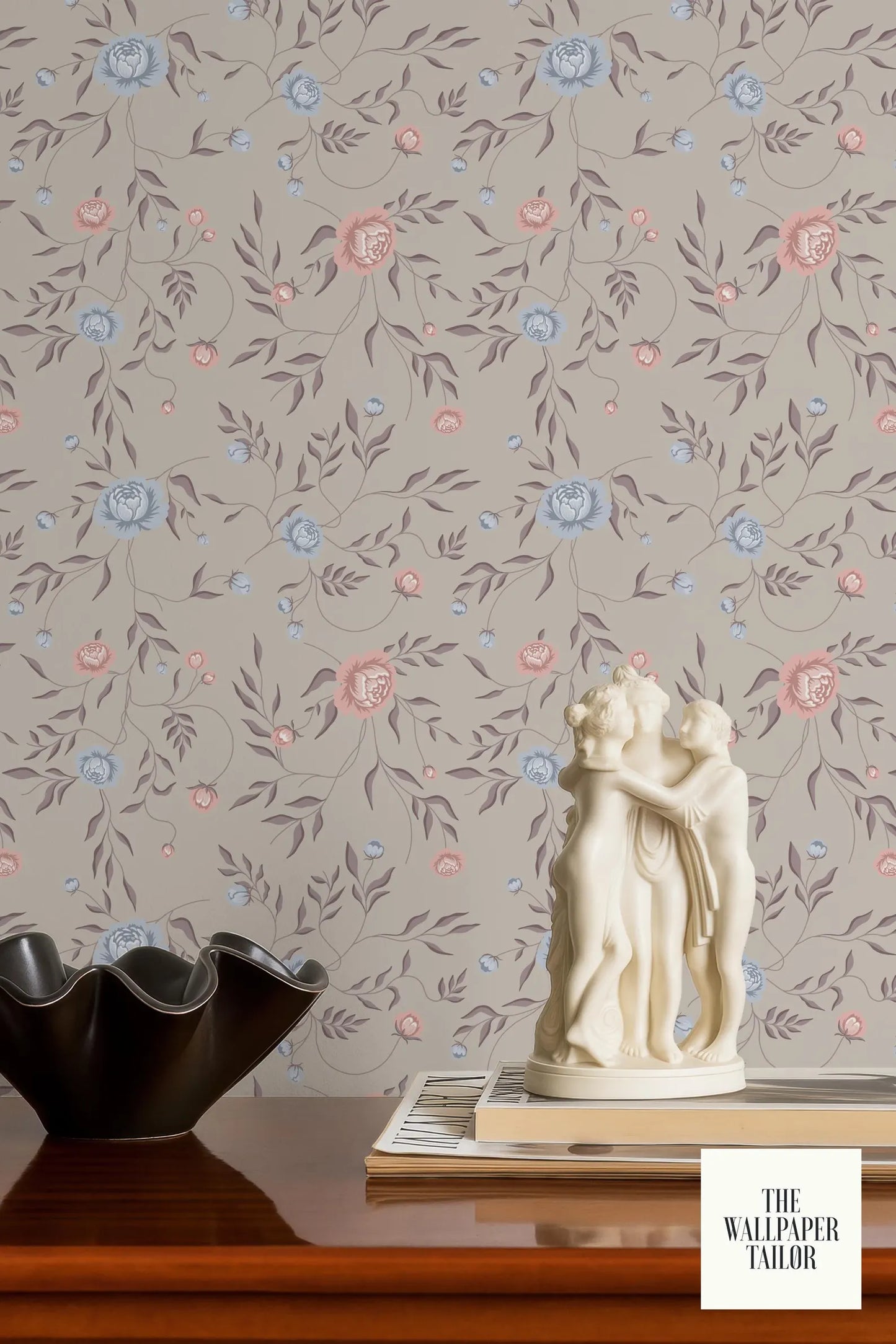 a decorative wallpapered wall with a floral pattern, a small white statue of two figures, and a black bowl on a wooden surface.