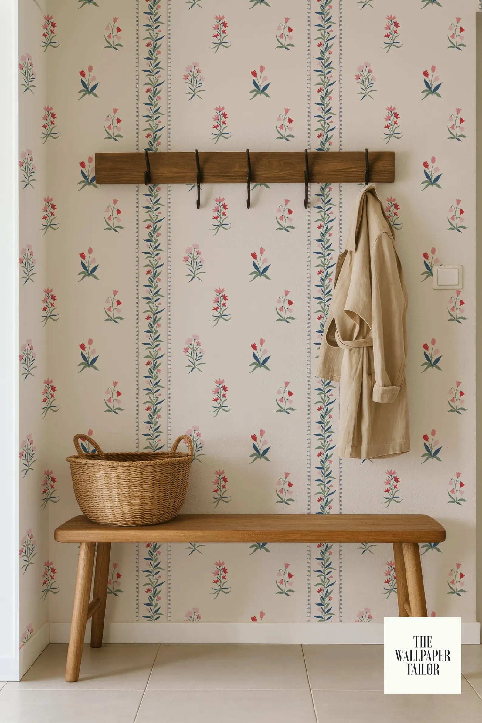 a wooden bench with a wicker basket on it, set against a wall with a floral wallpaper. A coat is hanging on a wooden rack above the bench.