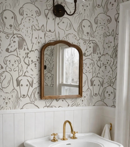 a bathroom with a white sink and a gold faucet, and a mirror above it. The wall behind the sink has a repeating pattern of dog faces, creating a playful and whimsical atmosphere.