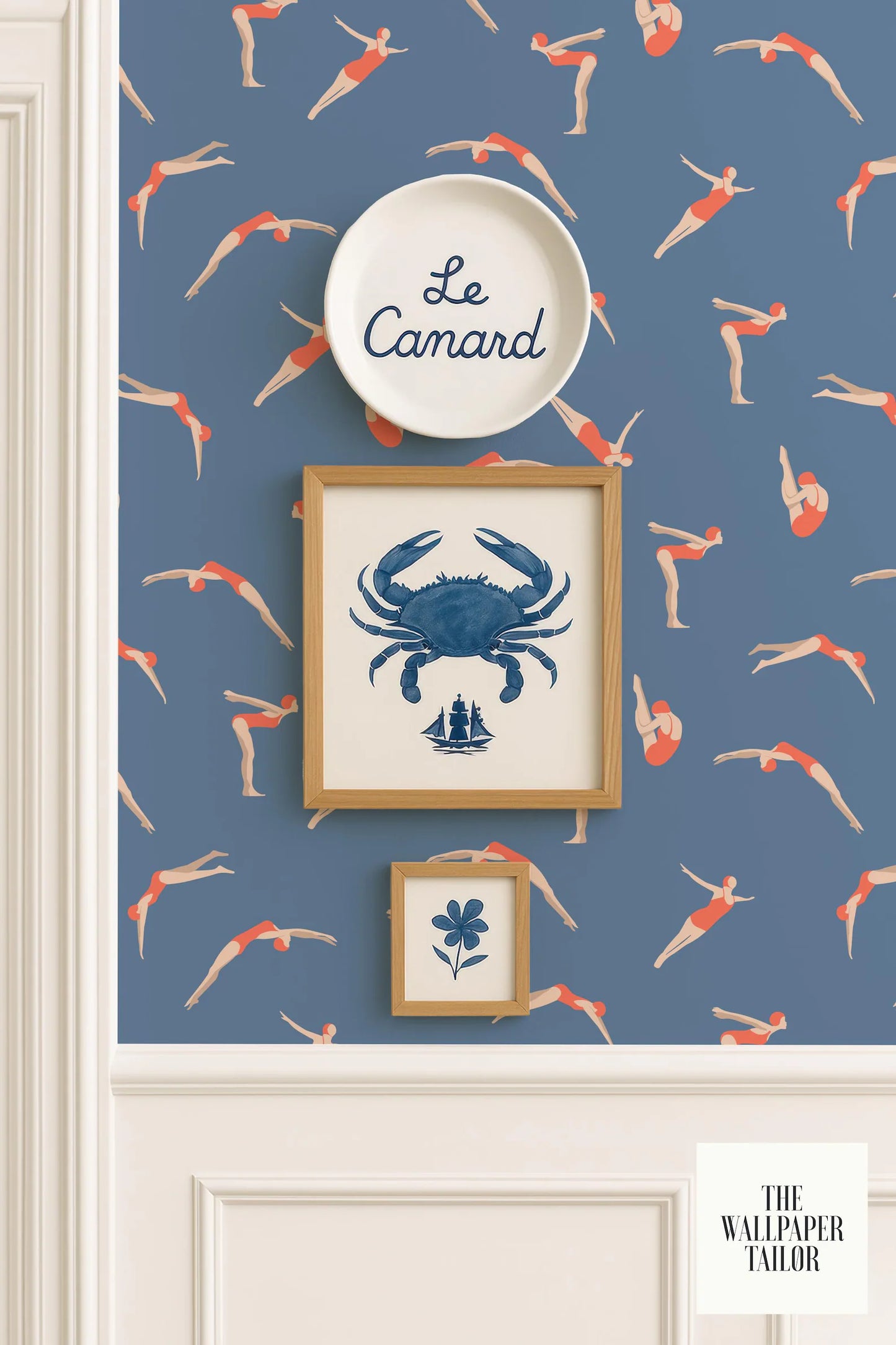 a wallpapered wall with a framed picture of a crab, a framed picture of a flower, and a plate with the word "Le Camard" written on it. The wall also has a pattern of swimming figures, and there is a small sign that reads "The Wallpaper Tailor".