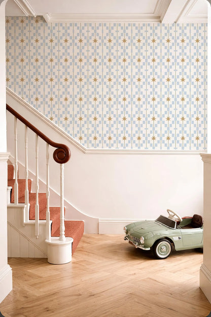 a vintage-style green toy car parked on a wooden floor next to a staircase with a white railing. The walls are adorned with a patterned wallpaper, and the overall color scheme is predominantly white and blue.