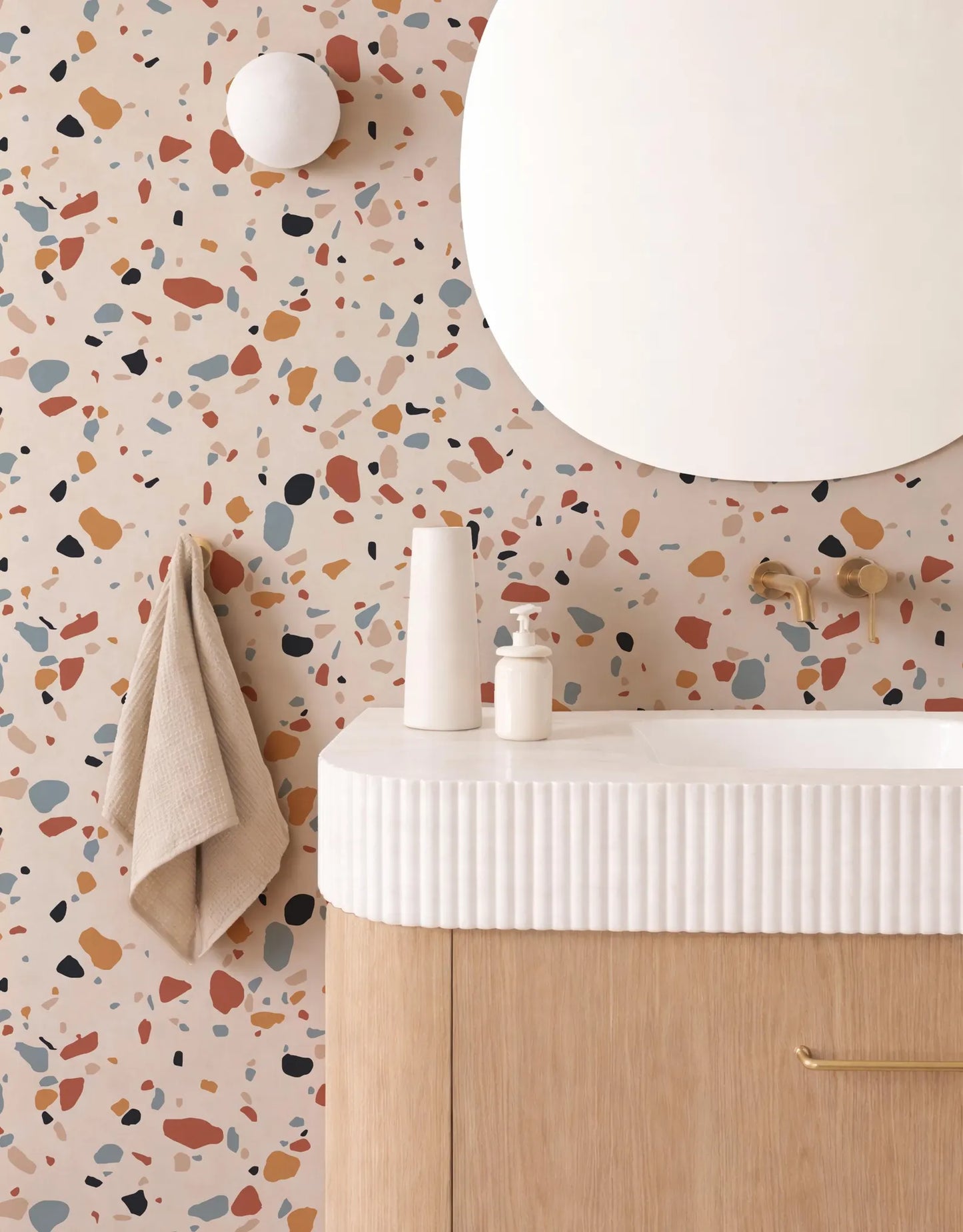 a bathroom with a white sink, a round mirror, and a colorful, speckled wall behind it.