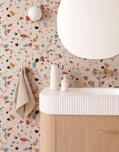 a bathroom with a white sink, a round mirror, and a colorful, speckled wall behind it.