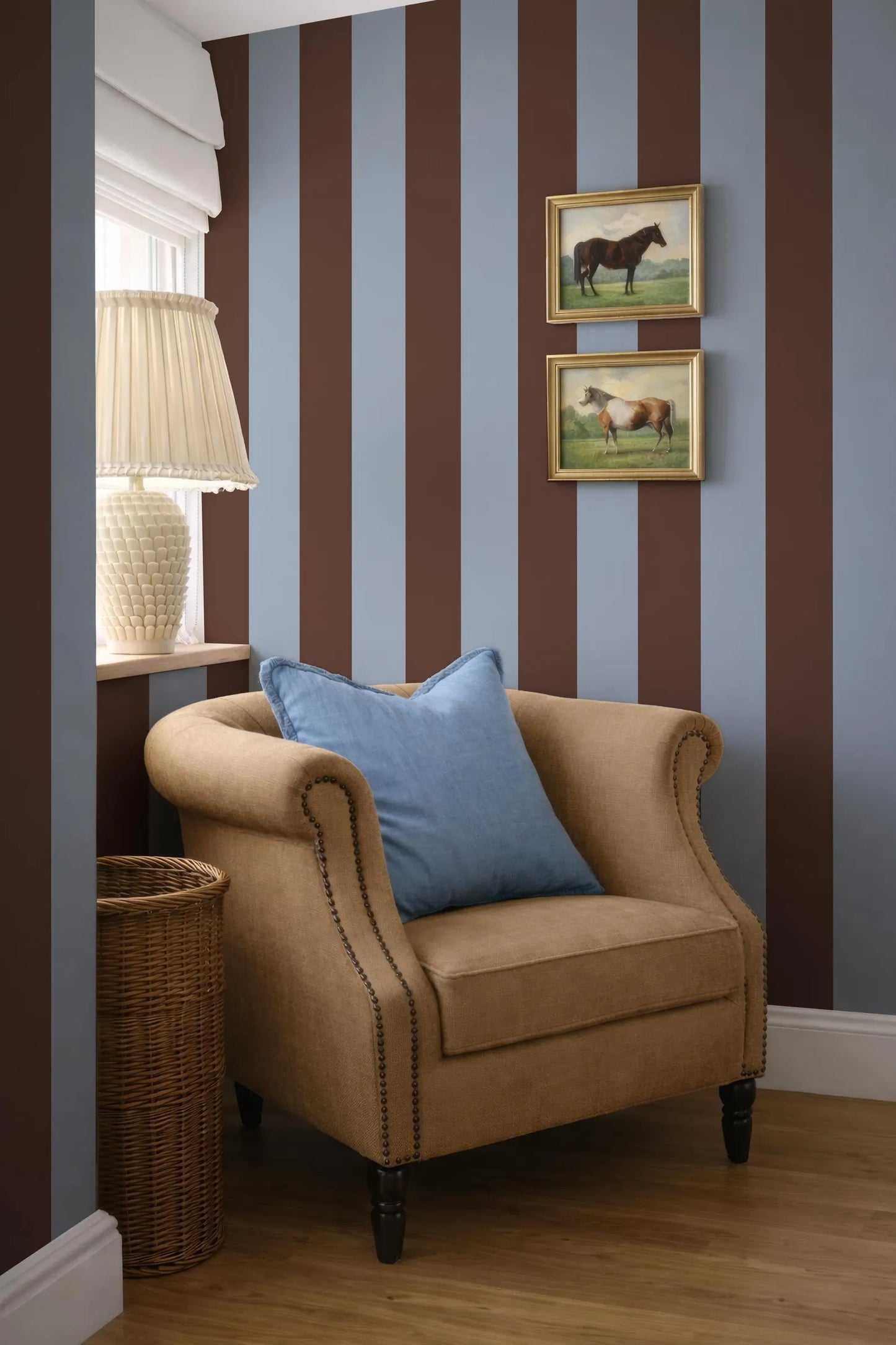 a cozy corner with a beige armchair, a wicker basket, and a framed picture of horses on the wall.