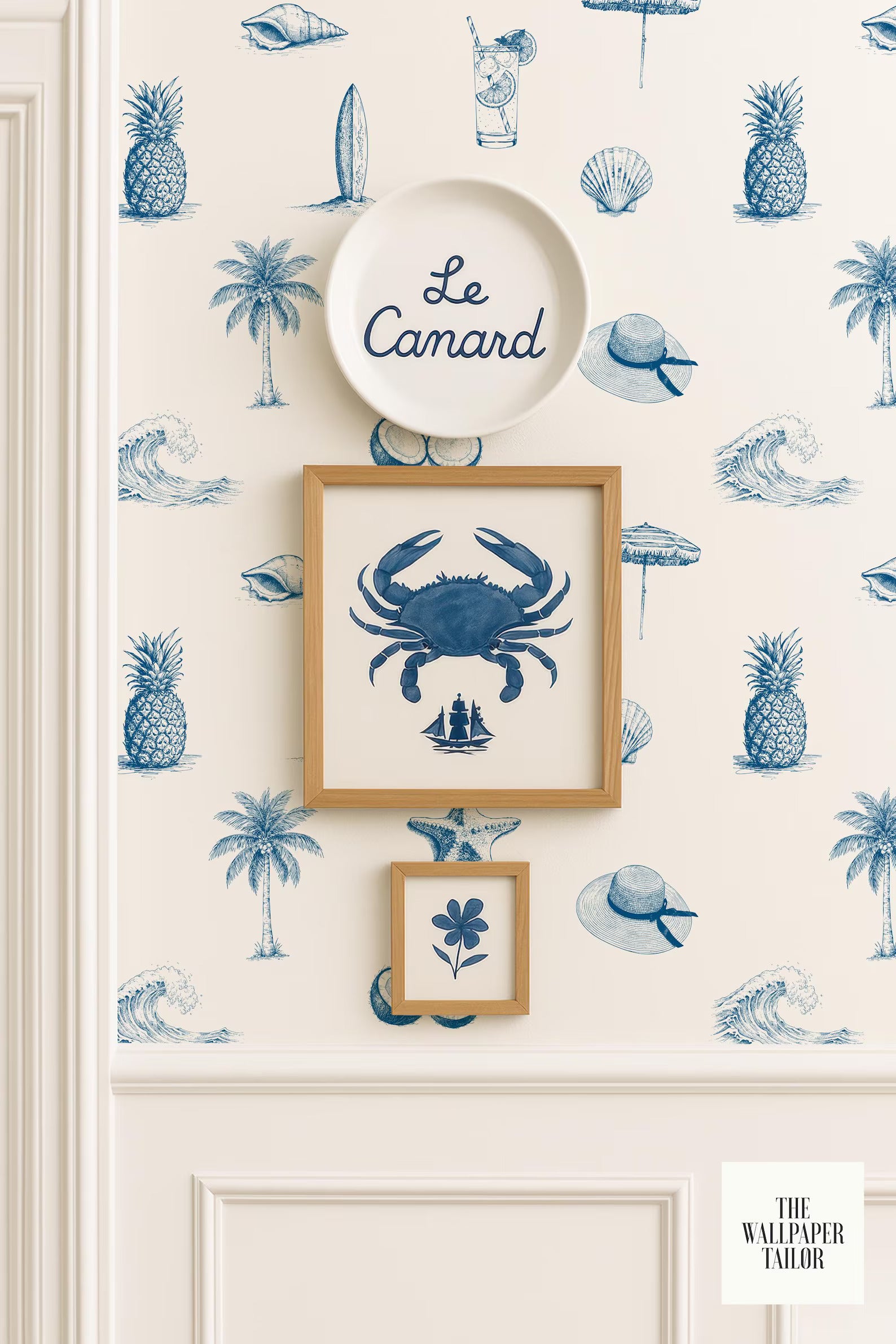 a wallpapered wall with a framed picture of a crab, a plate with the word "Camard" written on it, and a small framed picture of a flower. The wall also has a repeating pattern of blue palm trees and other tropical elements, such as a surfboard and an umbrella.
