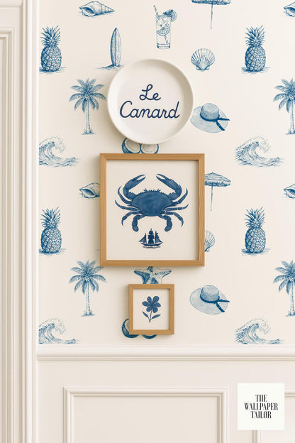 a wallpapered wall with a framed picture of a crab, a plate with the word "Camard" written on it, and a small framed picture of a flower. The wall also has a repeating pattern of blue palm trees and other tropical elements, such as a surfboard and an umbrella.