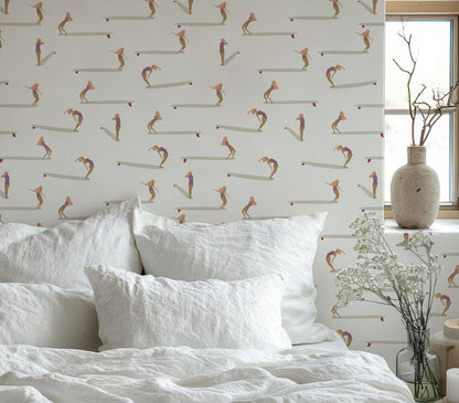 a bedroom with a white bed and a wallpapered wall with a repeating pattern of people surfing. There is also a vase with flowers on the windowsill.