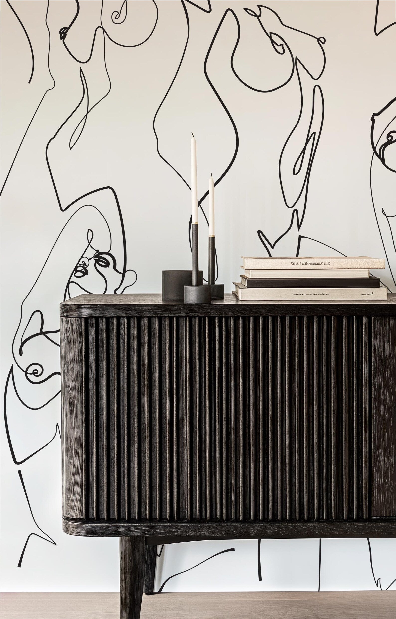 a dark wooden cabinet with a sleek, modern design. The cabinet has a sleek, curved front and a dark finish, giving it a sophisticated and stylish appearance. In front of the cabinet, there are two candles and a stack of books, adding a touch of warmth and personality to the space. The background of the image is a white wall adorned with abstract black lines, which creates a striking contrast and adds depth to the overall composition.