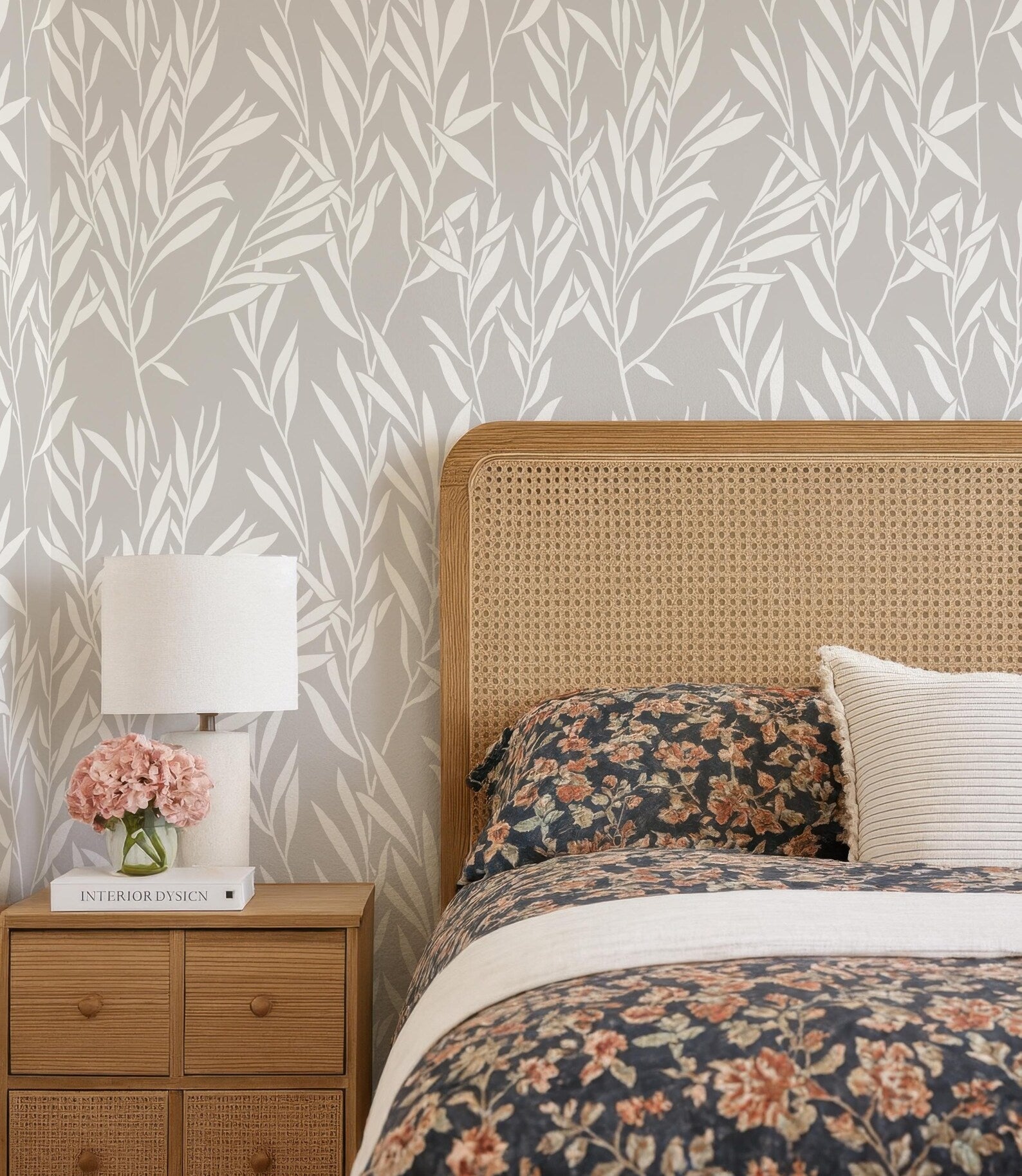 a bedroom with a floral bedspread, a wooden headboard, and a wooden nightstand with a lamp and a book.