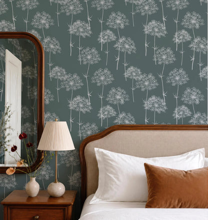 a bedroom setting with a bed, nightstand, and lamp. The bed has white pillows and a brown pillow, and the wall behind the bed has a patterned wallpaper with white flowers. The nightstand has a lamp on it, and there is a vase with flowers on the nightstand.