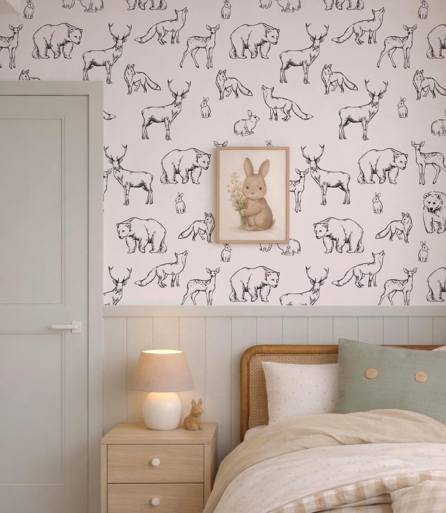 a bedroom with a wallpapered wall that has a repeating pattern of black and white animal illustrations, including bears, deer, and rabbits. Above the bed, there is a framed picture of a rabbit. The room also includes a bed with a wooden headboard, a nightstand with a lamp, and a door.