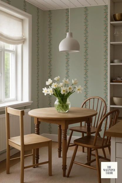a cozy dining area with a wooden table, two chairs, and a vase of white flowers on the table. The walls are adorned with a patterned wallpaper, and a white pendant light hangs above the table.