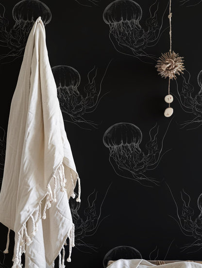 a black wall with a white towel hanging on a hook, a hanging ornament, and a black and white illustration of jellyfish on the wall.