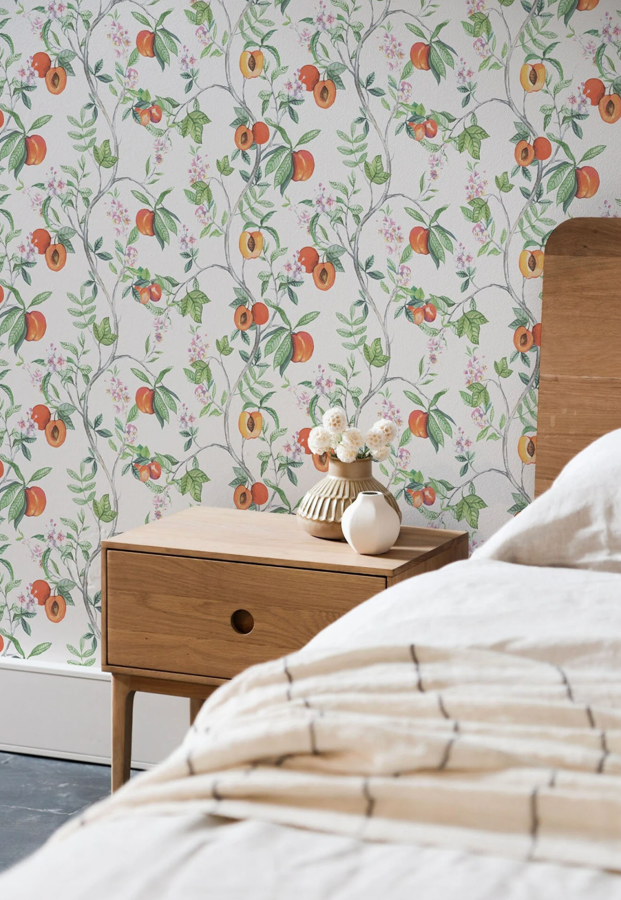 a bedroom with a wooden nightstand, a floral wallpaper, and a white bed with a striped blanket.