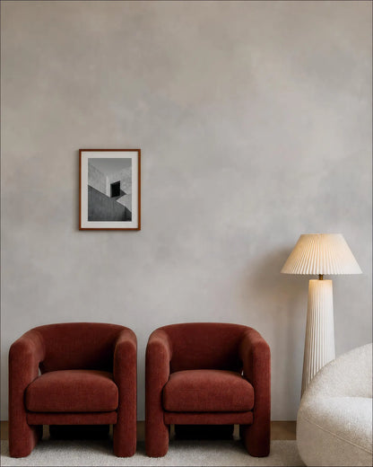 a minimalist living room with two red armchairs, a white floor lamp, and a framed black and white photograph on the wall.