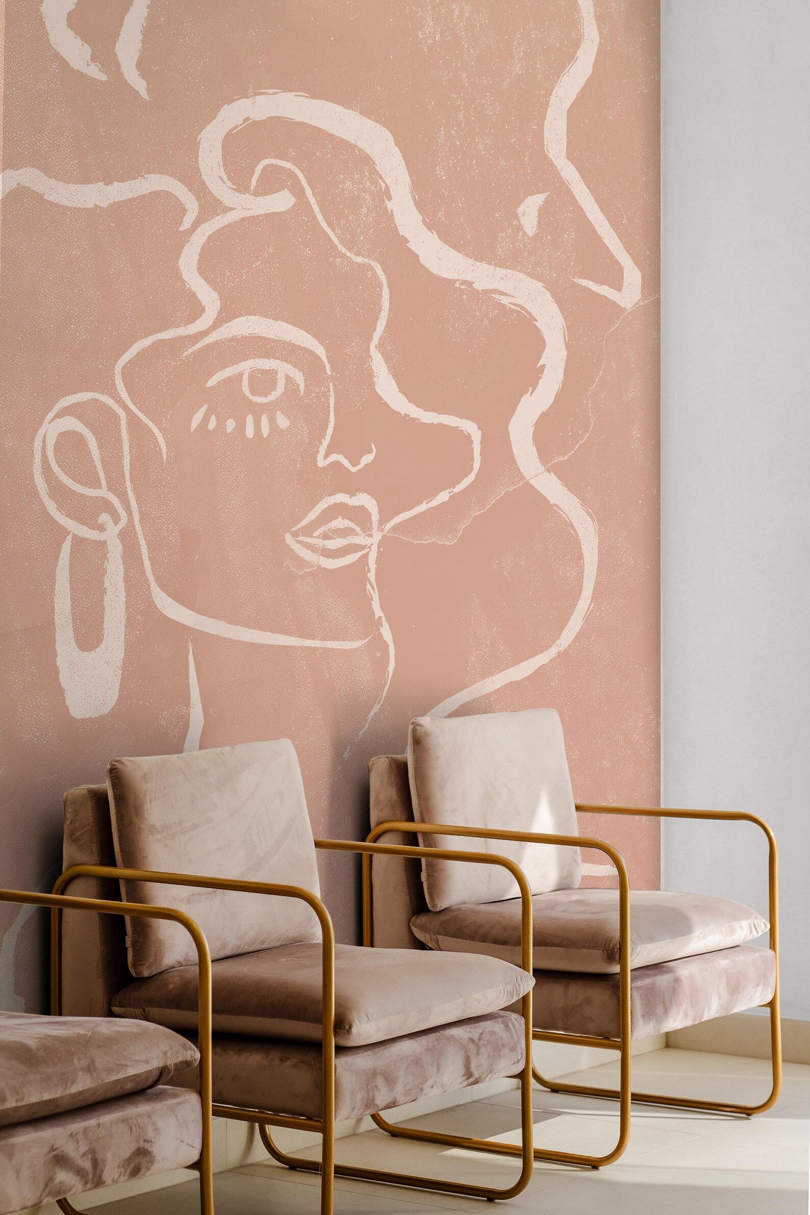 a wall with a large abstract face painted on it, and there are three beige chairs with gold frames placed in front of the wall.