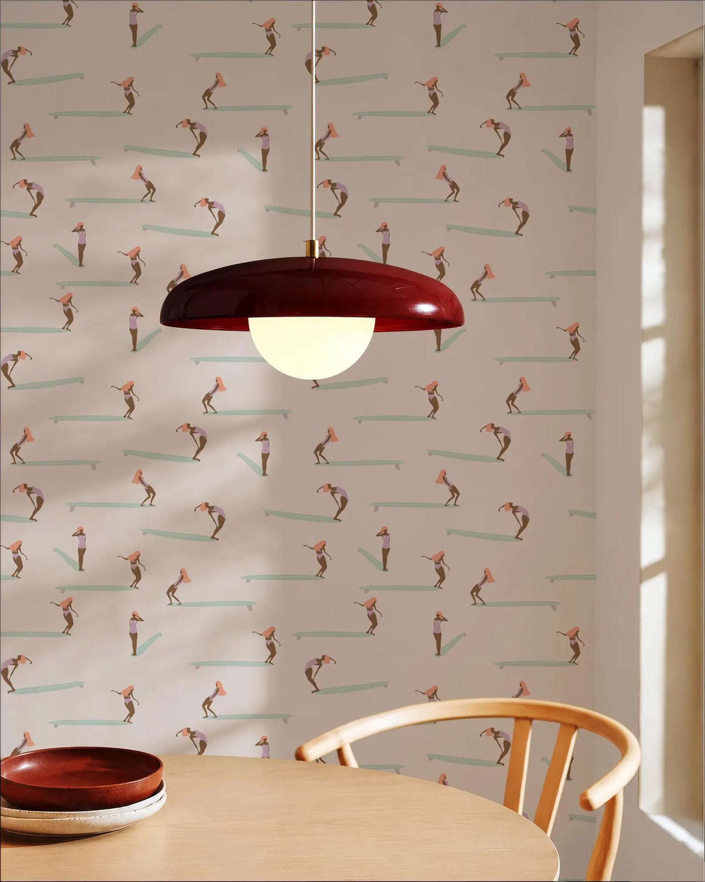 a dining area with a wooden table and chair, a red pendant light hanging above the table, and a patterned wallpaper with a repeating design of surfers on a wave.