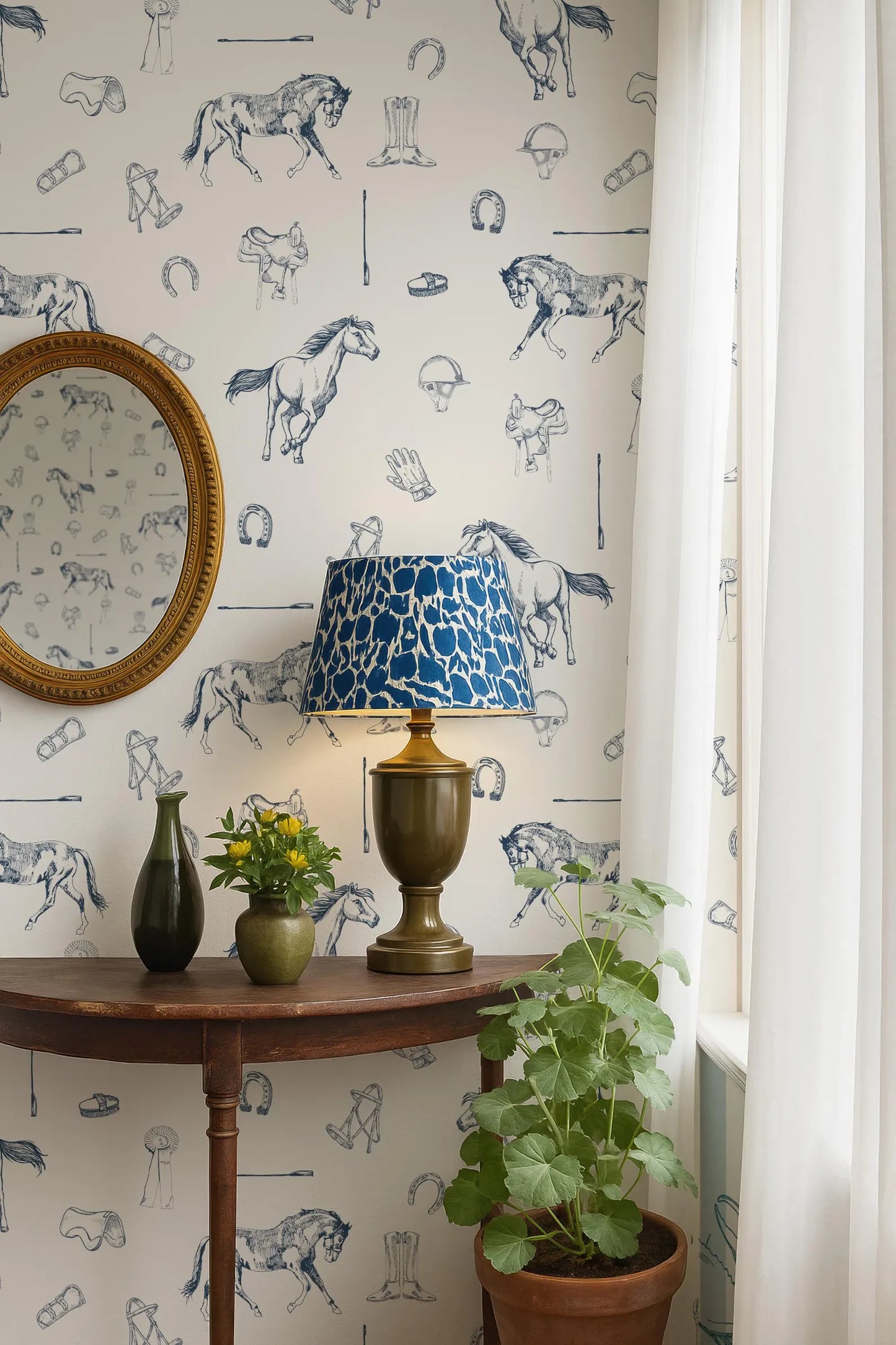 a room with a wooden table, a lamp with a blue and white patterned lampshade, a round mirror, a potted plant, and a vase with flowers. The wall behind the table has a wallpaper with various horse illustrations.