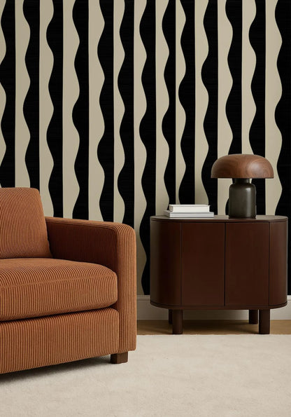 a modern living room with a brown sofa, a wooden side table, and a lamp on top of the side table. The wall behind the furniture has a black and white striped pattern.