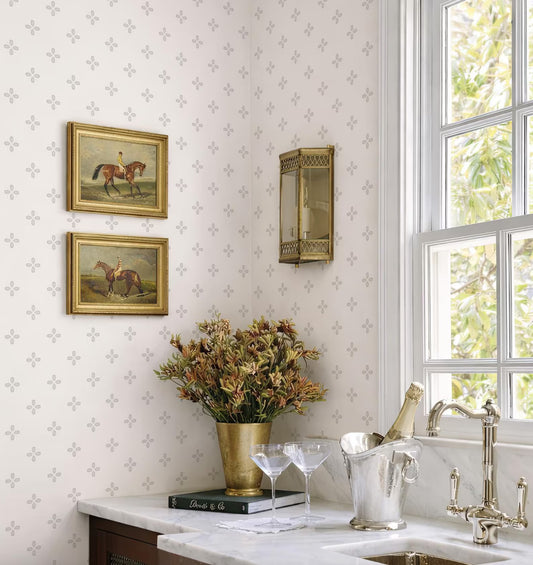 a cozy and elegant kitchen corner with a white marble countertop, a vase of flowers, a wine glass holder, and a book. The wall behind the countertop has a patterned wallpaper, and there are two framed paintings hanging on the wall.