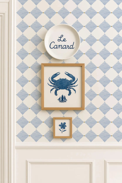 a wall with a blue and white diamond pattern wallpaper, and there are three framed pictures hanging on it. The top picture is a blue crab, the middle picture is a small blue flower, and the bottom picture is a blue and white diamond pattern.