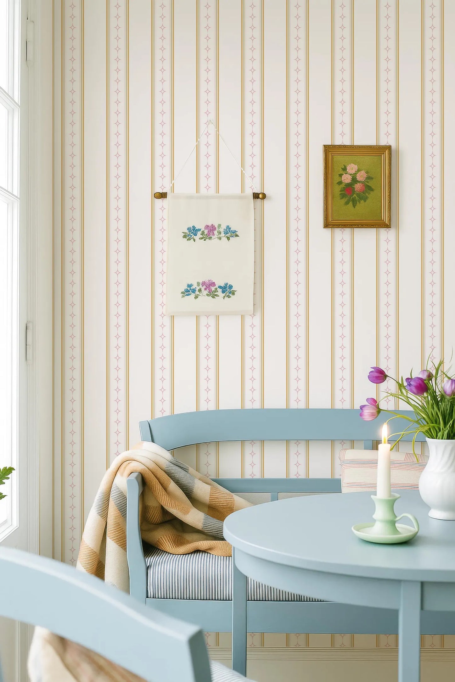 a cozy and charming living room with a blue bench, a table with a candle, and a framed picture on the wall. The room has a striped wallpaper and a window, creating a warm and inviting atmosphere.