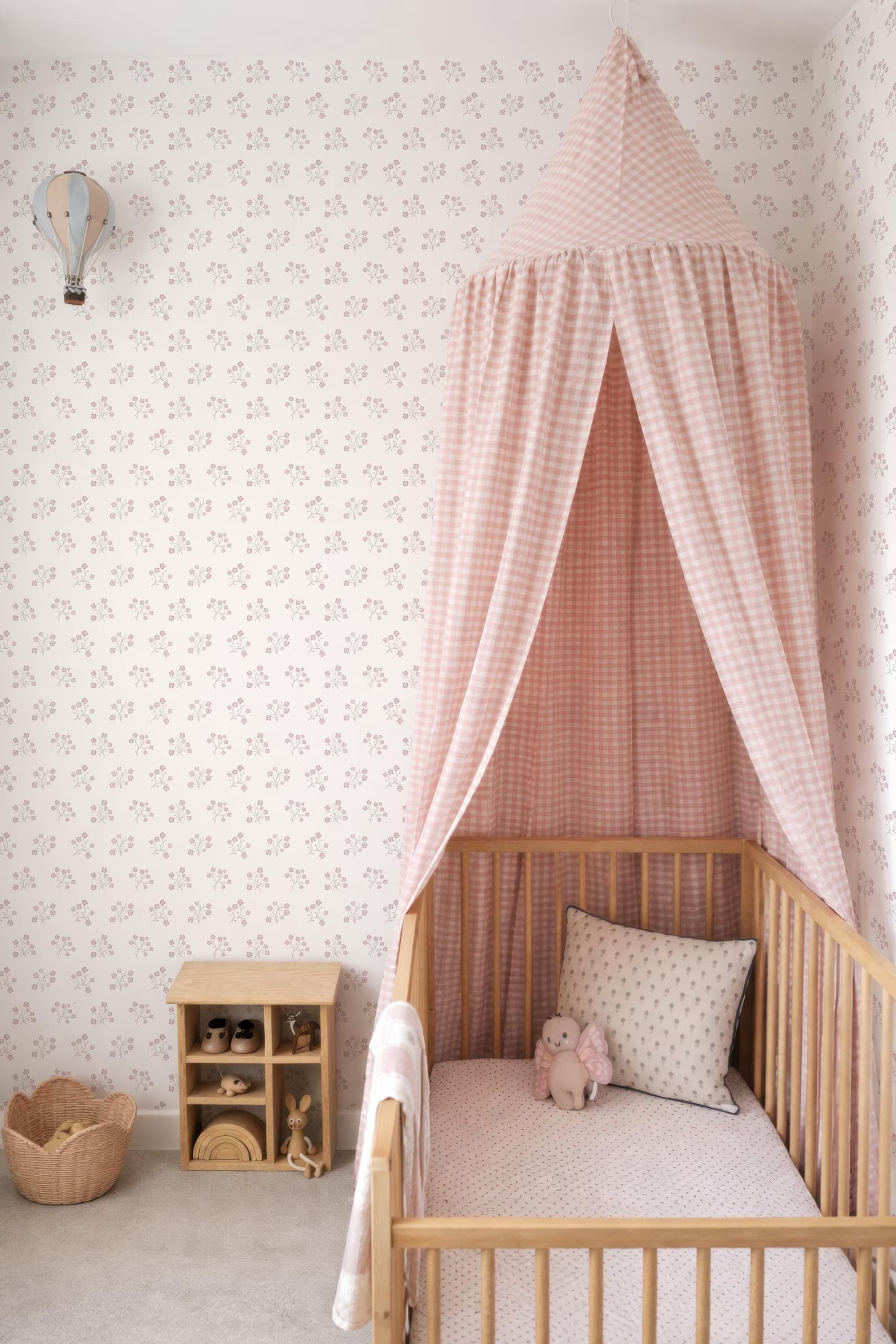 A cozy nursery with a wooden crib, a canopy bed, and a wooden toy shelf. The walls are decorated with a floral pattern, and there is a small basket on the floor.