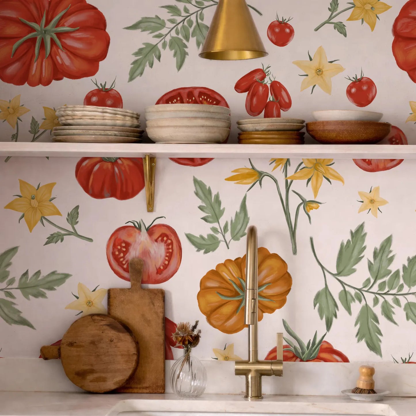 a kitchen counter with a variety of kitchen items, including a wooden cutting board, a vase with flowers, and a sink with a gold faucet. The wall behind the counter is decorated with a vibrant tomato and flower pattern, creating a lively and colorful atmosphere in the kitchen.