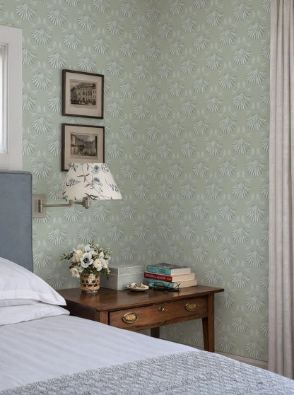 a cozy bedroom scene with a bed, a wooden nightstand, and a lamp. The walls are covered in a patterned wallpaper, and there are two framed pictures hanging above the bed. The nightstand has a vase of flowers and a stack of books on it.