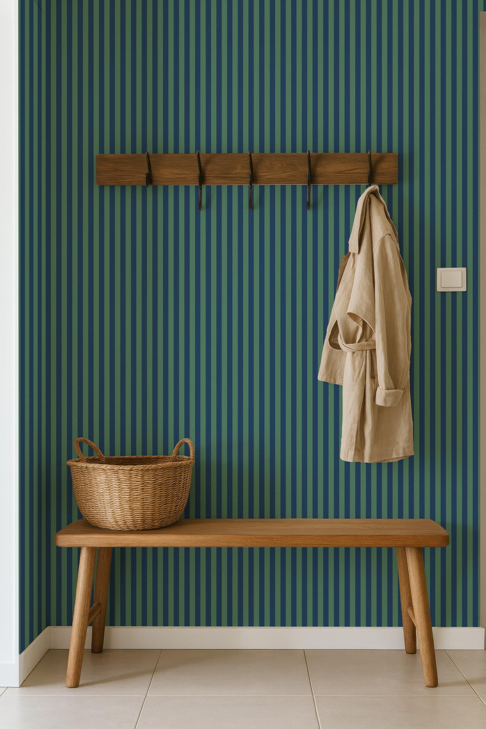 a wooden bench with a wicker basket on it, set against a striped green and blue wall. A coat is hanging on a wooden coat rack above the bench.