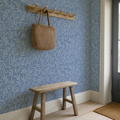a blue wall with a leafy pattern, a wooden bench, and a woven bag hanging on a wooden rack.
