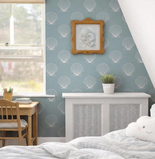 a cozy bedroom with a blue and white color scheme, featuring a framed picture of a shell on the wall, a wooden desk, a white radiator, and a comfortable bed with a cloud-shaped pillow.