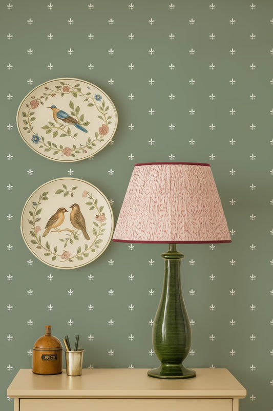 a green lamp with a pink lampshade, a wooden jar, and two decorative plates with birds on them, all set against a green wall with white stars.
