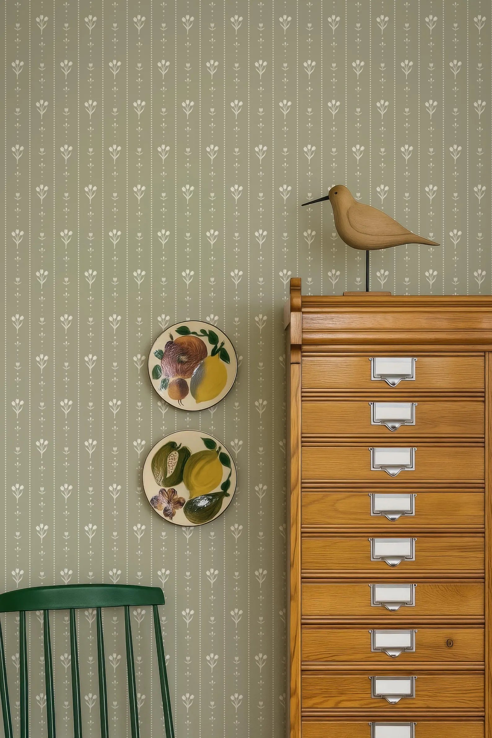 a wooden cabinet with multiple drawers, a green chair, and two decorative plates on the wall.