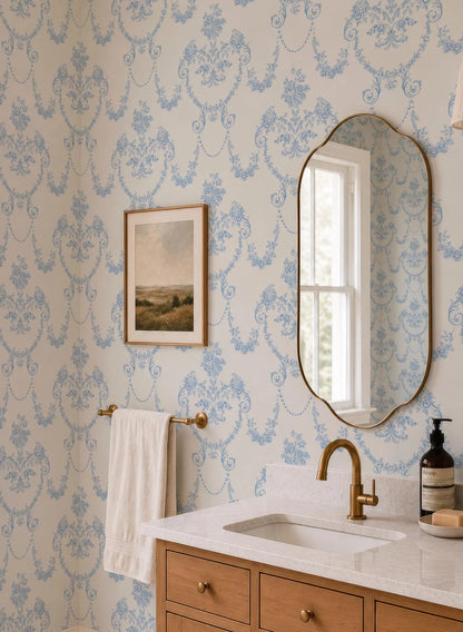 a bathroom with a white sink, a mirror, and a towel rack. The walls are covered in blue floral wallpaper, and there is a painting hanging above the mirror.