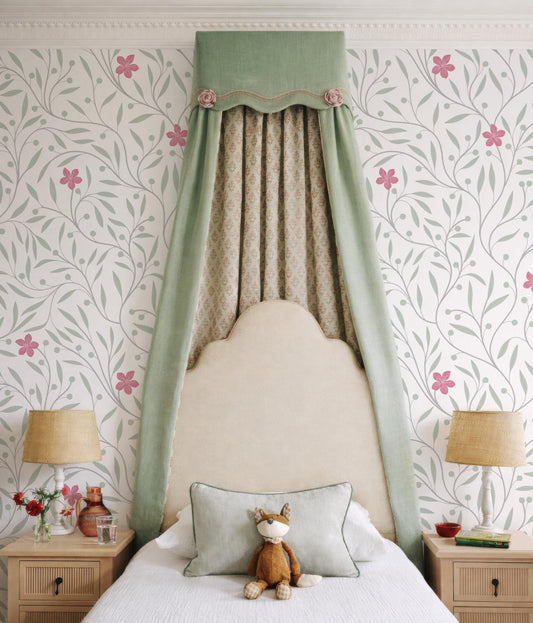 a cozy bedroom with a white bed, a green curtain, and a lamp on a nightstand. A stuffed animal is placed on the bed, and the walls are decorated with a floral pattern.