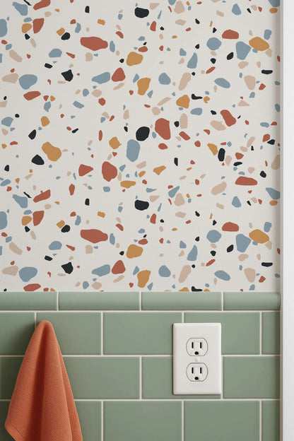a wall with a colorful, speckled pattern, likely a tile or wallpaper design, and a green tile border below it. There is also a white electrical outlet visible on the wall.