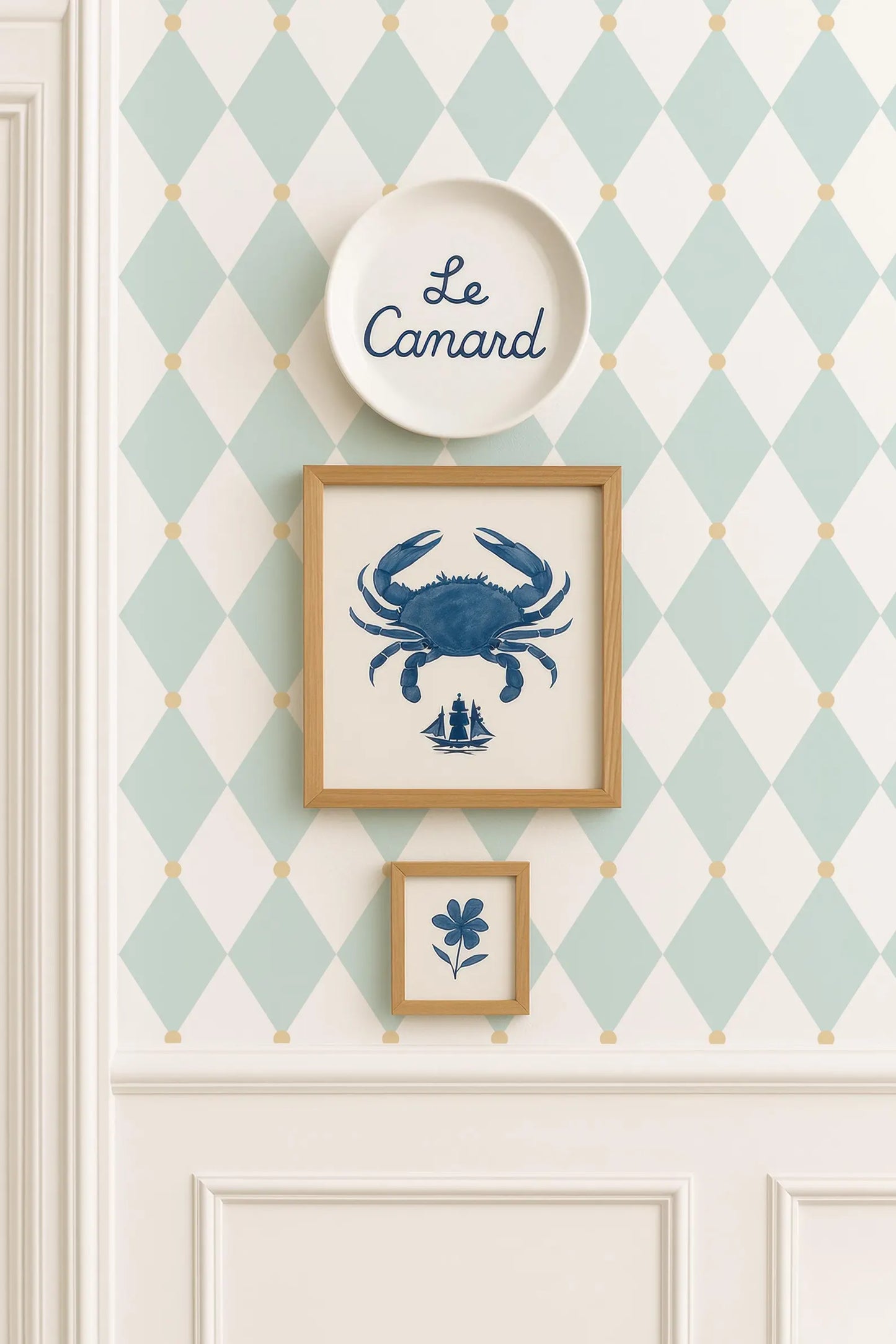 a wall with a diamond pattern wallpaper, a white plate with the word "Camard" written on it, and two framed pictures hanging on the wall.